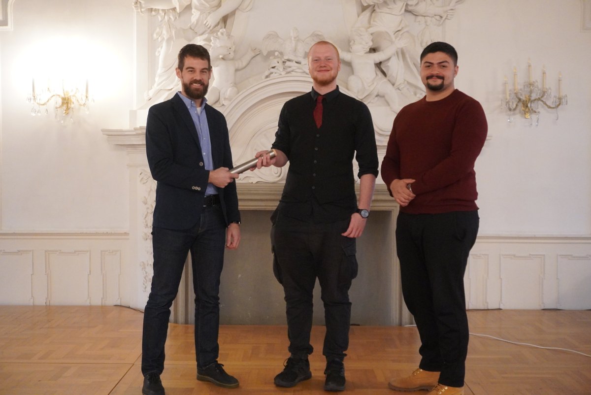 Das Bild zeigt, wie der SMV-Mitarbeiter des SG 42.1,  Jens Kußmann, den Staffelstab an den neuen Bezirksschülersprecher John Reinhardt (Staatliche Berufsschule Lichtenfels) übergibt. Rechts im Bild ist der stellvertretende Bezirksschülersprecher Hartmut Krings (Staatliche Berufsschule Hof) zu sehen.
